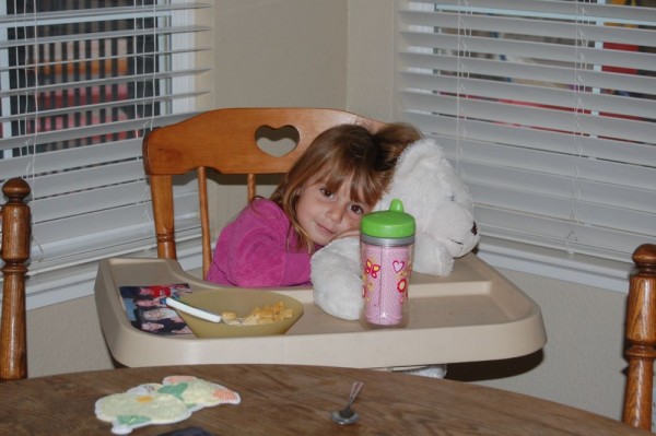 Cereal in a highchair she was too big for.. with a giant bear and a pic of her cousins